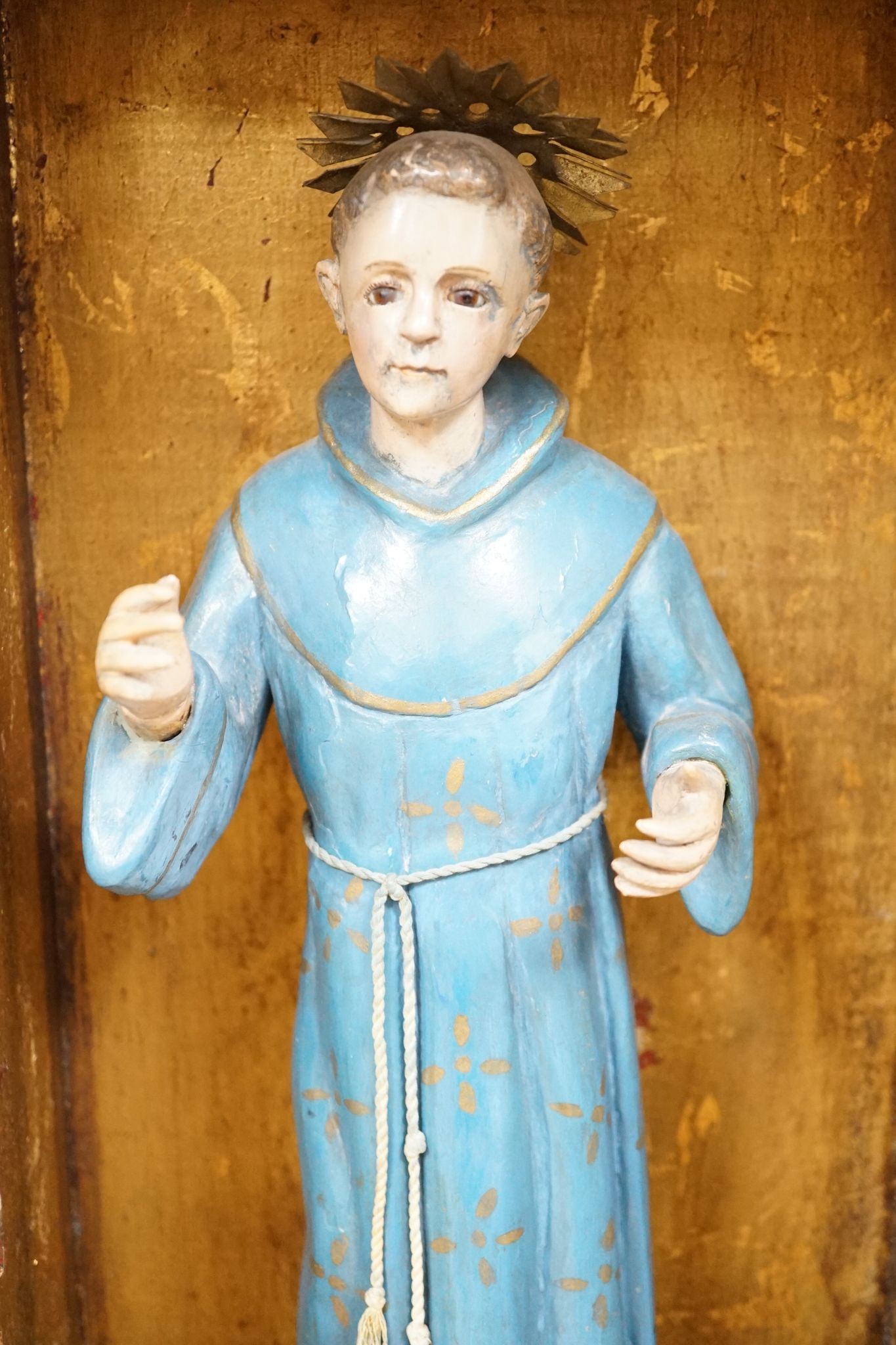 A painted saint with a blue robe and gilt metal halo, standing in an ornate carved niche, 57cm